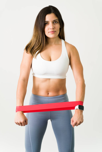 Femme athlétique avec une bande de résistance. Portrait d'une jeune femme en forme et mince avec des abdos forts tenant une bande de fitness pour exercer les muscles de sa poitrine - Photo, image