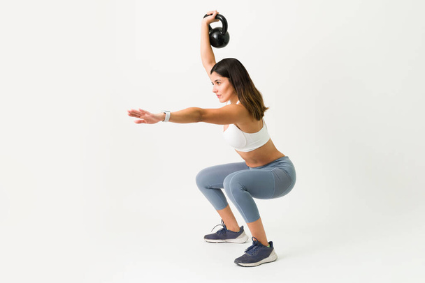 Squats exercises with a kettlebell. Strong caucasian woman squatting while holding a kettlebell weight to workout her arms, legs and back - Foto, Bild