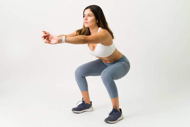 Squats sont le meilleur exercice pour vos jambes. Fitness femme mince en vêtements de sport faire une séance d'entraînement squat sur un fond blanc  - Photo, image