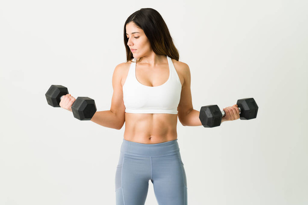Mujer fuerte con un cuerpo musculoso levantando dos pesas de pesa. Atractiva mujer deportiva en ropa deportiva trabajando su cuerpo atlético  - Foto, Imagen