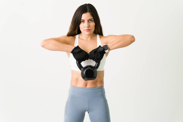 Work hard to have a strong body. Gorgeous young woman working out her biceps and back with a kettlebell weight  - Photo, Image