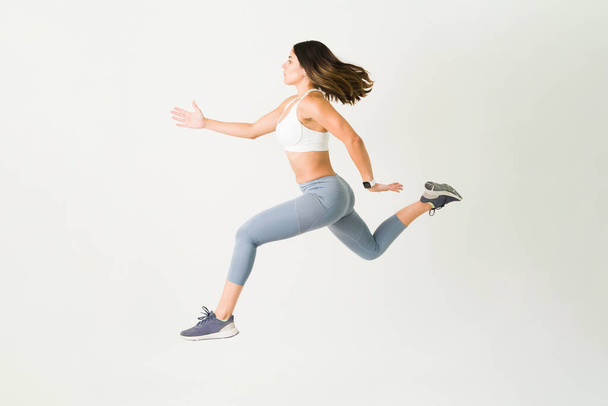 Aktywna młoda kobieta w sportowej odzieży skacząca w powietrzu. Sportowy sportowiec o silnym oporze wykonujący trening wytrzymałościowy i trening HIIT - Zdjęcie, obraz