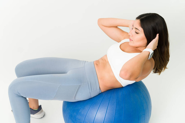 Angle élevé d'une jeune femme en tenue sportive faisant des redressements assis sur un ballon d'exercice. Femme en forme active exerçant son abdomen tonique - Photo, image