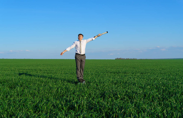 empresário posa com um spyglass em um campo verde, ele olha uma ideia ou algo assim, conceito de negócio, grama verde e céu azul como fundo - Foto, Imagem