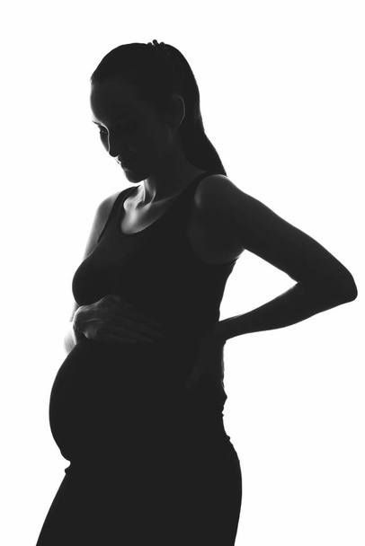 Silhouette Porträt einer schwangeren Frau auf weißem Hintergrund mit den Händen auf dem Bauch, vertikales Bild, ivf Schwangerschaftskonzept - Foto, Bild