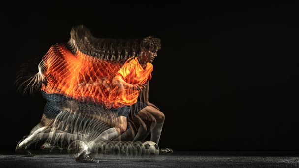 One Caucasian football soccer player in motion and action in mixed light on dark background. - Фото, изображение