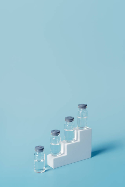 Various vials with liquid placed on steps on a blue background. Concept of medicine and coronavirus. vertical image with copy space. - Foto, Imagem
