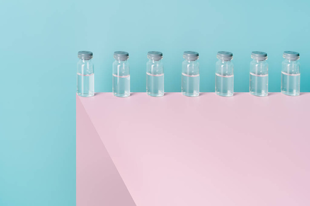 frascos con líquido sobre una estructura rosa y un fondo azul. Concepto de medicina y coronavirus. espacio de copia - Foto, Imagen