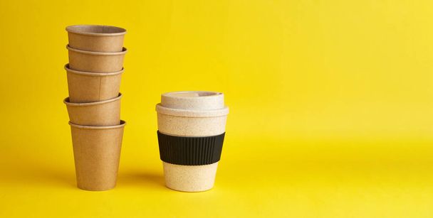 廃棄物ゼロの近代的な方法。使い捨ての紙コップの多くに対して1つの再利用可能な竹カップ。コーヒーと生態学。コピースペース付きイエローバナー - 写真・画像
