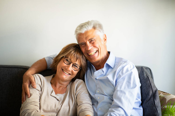 Close up portrait smiling happy older couple sitting on sofa together  - 写真・画像