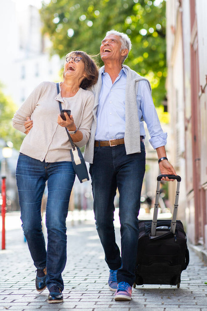 Full body portrait smiling couple walking with suitcase on street - Photo, Image