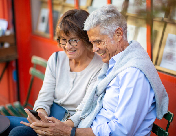 Portrait deux personnes âgées souriantes assis à l'extérieur regardant le téléphone mobile - Photo, image