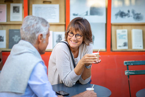 Portret lachende oudere vrouw zitten met man buiten houden drankje - Foto, afbeelding