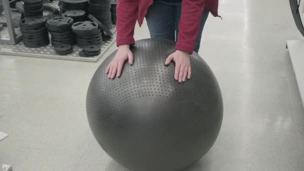 Kobieta w sklepie kupuje fitball. Dotyka jej dłońmi testując jej siłę. - Materiał filmowy, wideo