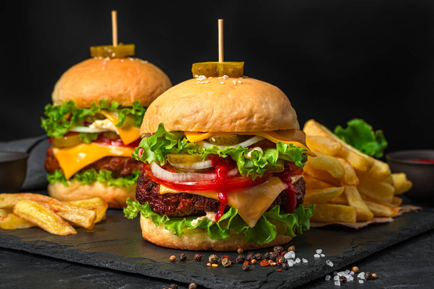 Zwei große saftige Hamburger und Pommes auf schwarzem Hintergrund. Fast food. - Foto, Bild