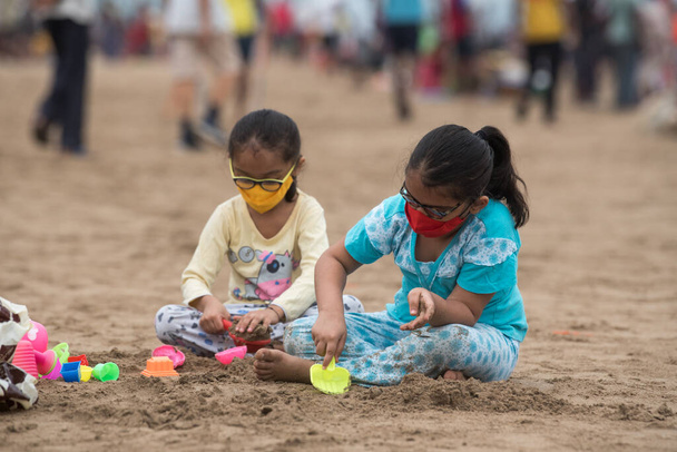 MUMBAI/INDIA - October 11, 2020: Children wearing mask playing at the Juhu beach after the government eased a lockdown restriction as a preventive measure against the COVID-19 coronavirus. - Photo, Image
