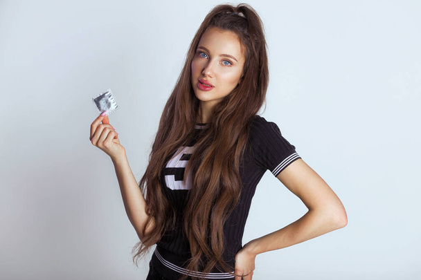 Безпечна концепція сексу. Красива молода жінка з довгим волоссям тримає презерватив. Турбота про вашу безпеку або сексуальну освіту мокап ізольовано на сірому, простір для тексту
 - Фото, зображення