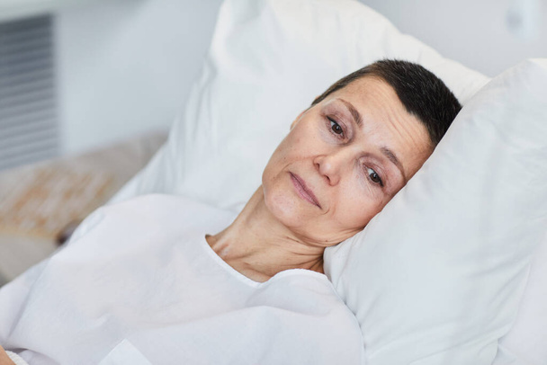 Θλιβερή ώριμη γυναίκα ξαπλωμένη στο κρεβάτι και αναρρώνει στο νοσοκομείο - Φωτογραφία, εικόνα
