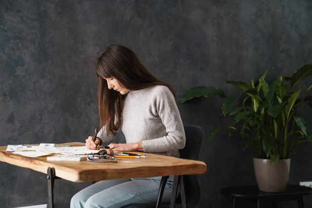 Serious beautiful calligrapher girl writing while working at table indoors - Fotó, kép