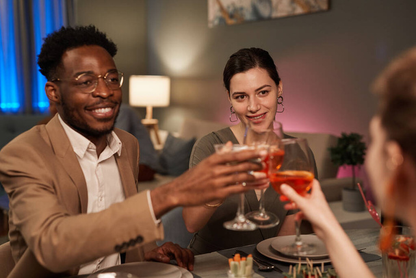 Retrato de una elegante pareja de razas mixtas disfrutando de la cena con amigos en el interior y brindando sobre la mesa festiva - Foto, Imagen