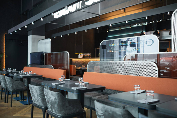Café à la mode avec des meubles gris et des panneaux de différentes formes entre les zones, planches en bois avec des lampes au-dessus des tables - Photo, image