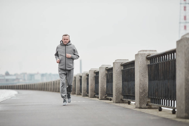 Doelgerichte oudere blanke man in grijs sportpak zwaaiende armen terwijl hij alleen liep in de koude ochtend - Foto, afbeelding