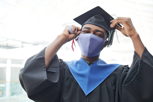 Waist up portrait of young African-American man wearing mask and graduation gown while smiling happily at camera indoors, copy space - Photo, Image