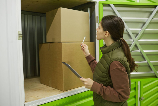 Young woman with documents packing boxes in storage - Foto, Bild