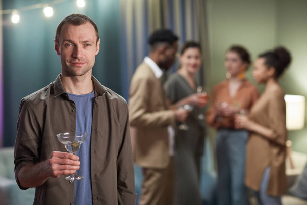 Waist up portrait of adult man looking at camera and holding cocktail glass while enjoying party at home, copy space - Foto, immagini