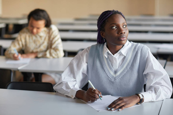 Portret van een jonge Afro-Amerikaanse vrouw die examen doet in het auditorium van de school en gepensioneerd wegkijkt, ruimte kopieert - Foto, afbeelding