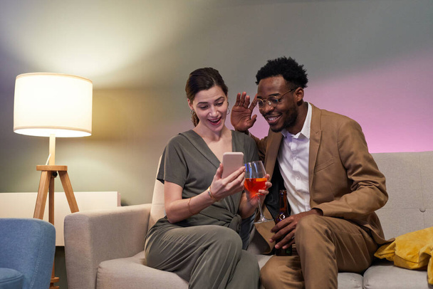 Retrato de pareja elegante saludando a la pantalla del teléfono inteligente mientras celebra en línea a través de chat de vídeo en el entorno de casa, espacio para copiar - Foto, imagen