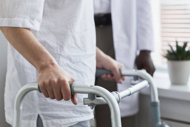 Close-up van de senior patiënt die met een looprek langs de ziekenhuisafdeling loopt - Foto, afbeelding