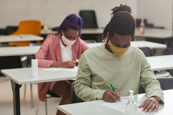 Портрет молодого афроамериканца в маске во время экзамена или экзамена в школе с дезинфицирующим средством для рук, копировальным пространством - Фото, изображение