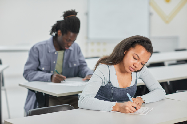 Schüler machen Test in der Schulklasse mit Fokus auf junge Afroamerikanerin sitzt am Schreibtisch vor, Kopierraum - Foto, Bild