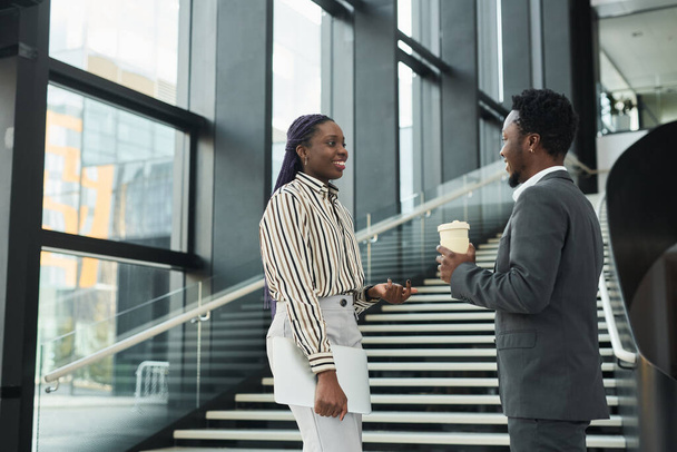 Graphic waist up portrait of two African-American business people chatting cheerfully while standing in office hall, copy space - Valokuva, kuva