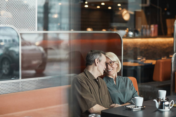Sorridente affettuoso anziano caucasico coppia seduta insieme sul divano e abbracciarsi mentre si guarda negli occhi di ogni altro in caffè - Foto, immagini