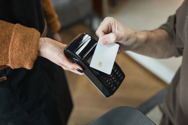 Primer plano del cliente irreconocible pagando con tarjeta sin contacto y poniéndolo en la terminal en poder de la camarera en la cafetería - Foto, imagen