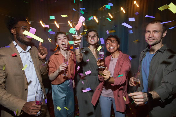 Grupo multiétnico de personas despreocupadas bailando en confeti mientras disfrutan de la fiesta en el interior, filmado con flash - Foto, imagen