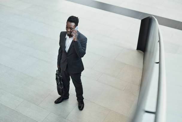 Vista de arriba hacia abajo en el exitoso hombre de negocios afroamericano hablando por teléfono inteligente en el salón de oficinas, espacio para copiar - Foto, Imagen