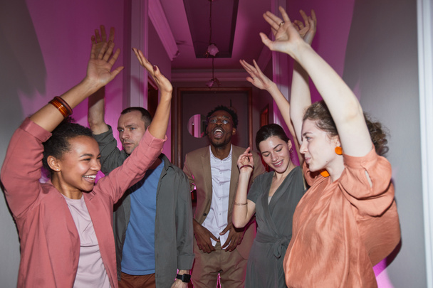 Разнообразная группа веселых людей, танцующих во время домашней вечеринки в помещении, снятая со вспышкой - Фото, изображение