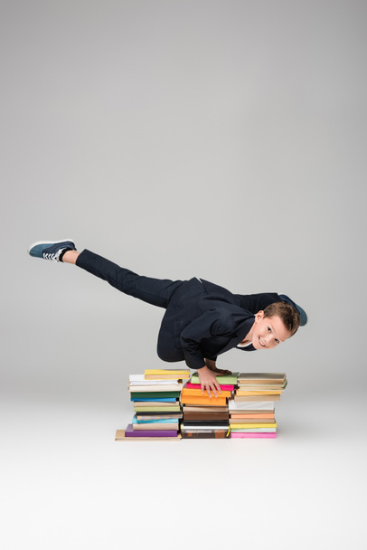 heureux écolier faire handstand sur pile de livres sur gris - Photo, image