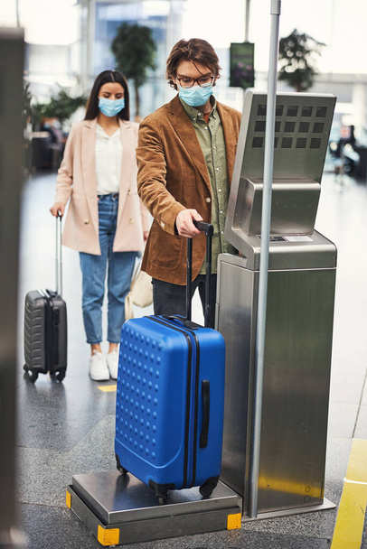 Pasajero masculino que utiliza una máquina de pesaje de control de equipaje en el aeropuerto - Foto, Imagen