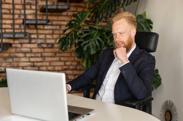 ノートパソコンを見つめスマートカジュアルなスーツで注目の赤髪のビジネスマン - 写真・画像