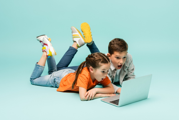 shocked children watching movie on laptop while lying on blue - Foto, imagen