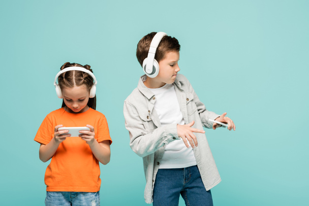 girl using smartphone near boy in wireless headphones listening music while dancing isolated on blue - Photo, Image