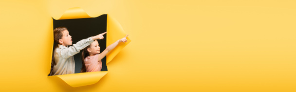 kids pointing away with fingers through hole on yellow background, banner - Photo, Image
