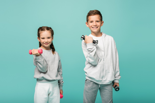happy kids in sportswear working out with dumbbells isolated on blue - Foto, afbeelding