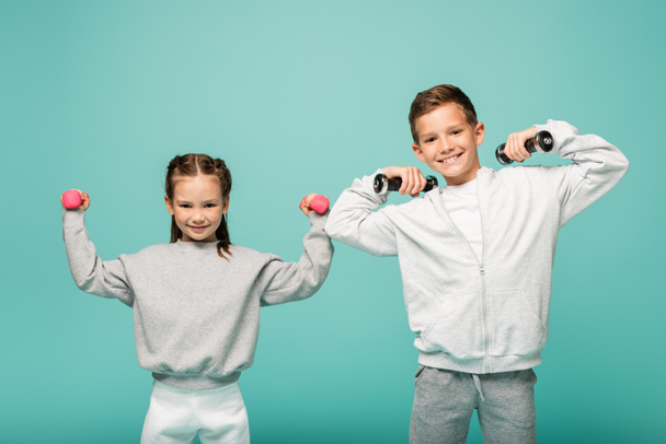 sportive kids in sportswear working out with dumbbells and smiling isolated on blue - Foto, immagini