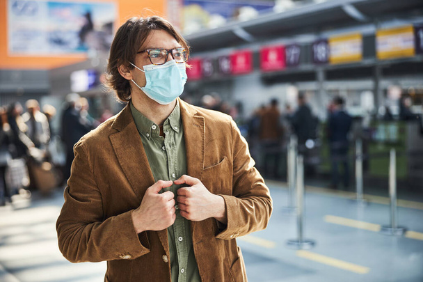 Stylischer Mann mit medizinischer Maske steht am Flughafen - Foto, Bild