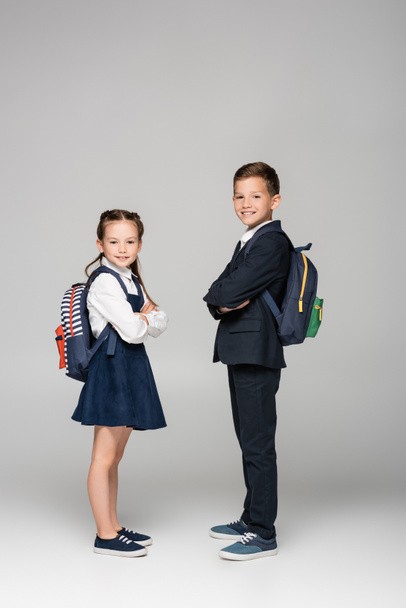 schoolchildren with backpacks posing with crossed arms on grey - Фото, зображення